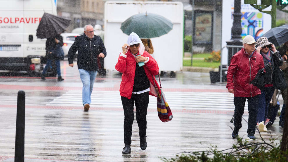 Varias personas tratan de cubrirse de la lluvia y el viento